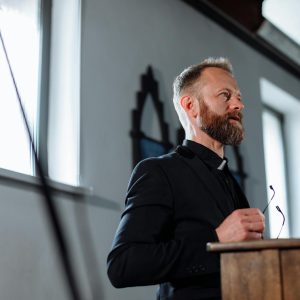 A priest passionately delivers a sermon from a pulpit inside a church.
